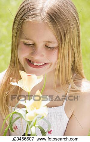 Stock Photo - Young girl standing outdoors holding blossom smiling. Fotosearch