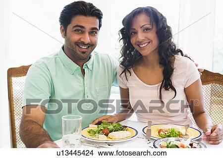Couple sitting at dinner table smiling (high key) View Large Photo Image Picture - Couple sitting at dinner table smiling (high key). Fotosearch