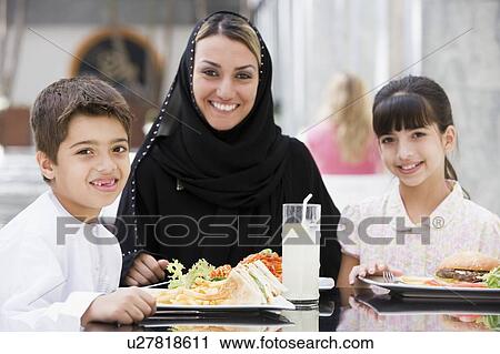 Stock Image - Family at restaurant eating and smiling (selective focus). Fotosearch