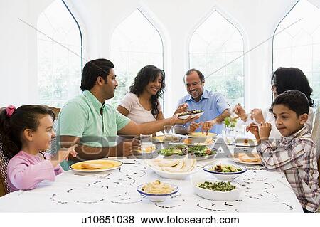 Stock Photo - Family sitting at dinner table smiling (high key). Fotosearch