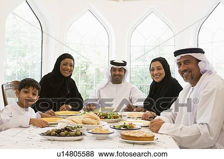 Stock Photo - Family sitting at dinner table smiling (high key). Fotosearch