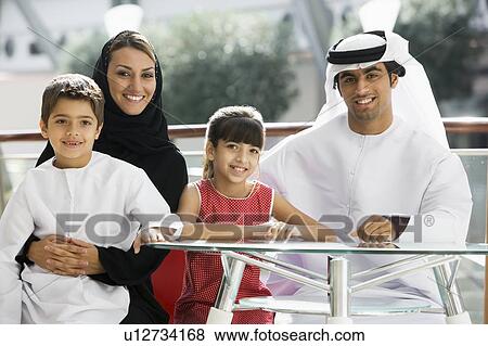 Family sitting indoors at table smiling (selective focus) View Large Photo Image Stock Photo - Family sitting indoors at table smiling (selective focus). Fotosearch