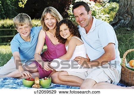 Stock Photo - Family sitting outdoors with picnic smiling. Fotosearch