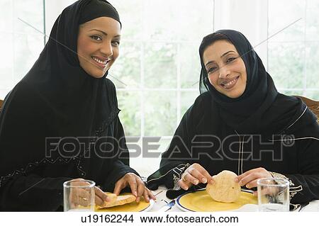 Two women sitting at dinner table smiling (high key) View Large Photo Image Picture - Two women sitting at dinner table smiling (high key). Fotosearch