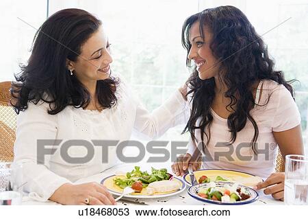 Stock Image - Two women sitting at dinner table smiling (high key). Fotosearch
