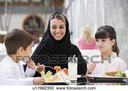 Stock Image - Woman and two young children at restaurant eating and smiling (selective focus). Fotosearch