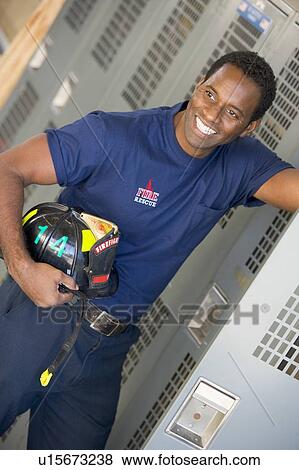 Fireman holding helmet standing by locker in fire station locker room (depth of field) View Large Photo Image Stock Photo - Fireman holding helmet standing by locker in fire station locker room (depth of field). Fotosearch