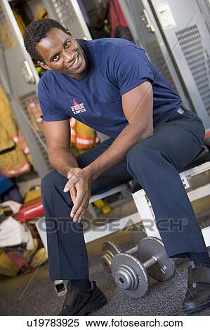 Stock Photography - Fireman sitting on bench in fire station locker room. Fotosearch