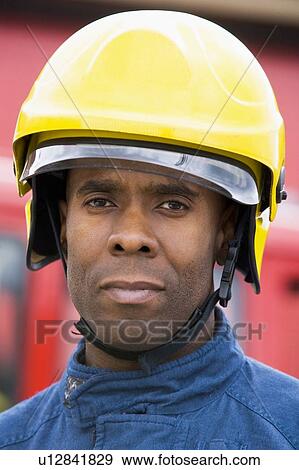 Stock Photo - Fireman standing by fire engine wearing helmet. Fotosearch