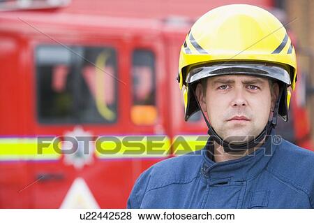 Stock Photo - Fireman standing by fire engine wearing helmet. Fotosearch
