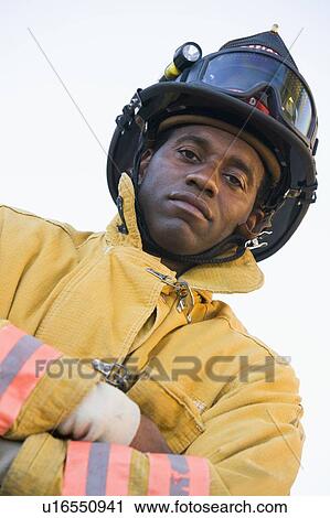 Stock Image - Fireman standing outdoors wearing helmet. Fotosearch