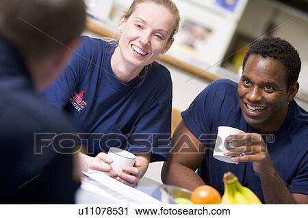 Stock Image - Three firefighters in break room drinking coffee and talking (selective focus). Fotosearch
