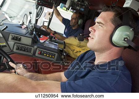 Picture - Two firemen in fire engine (selective focus). Fotosearch