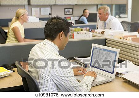 Stock Photograph - Businessman in cubicle at laptop. Fotosearch