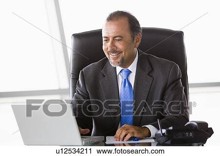 Stock Image - Businessman in office with laptop smiling (high key/selective focus). Fotosearch