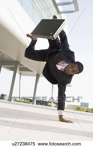 Stock Photography - Businessman outdoors by building standing on one hand. Fotosearch