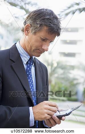 Stock Photo - Businessman outdoors using personal digital assistant. Fotosearch