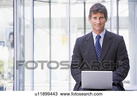 Businessman sitting in office lobby using laptop smiling View Large Photo Image Stock Image - Businessman sitting in office lobby using laptop smiling. Fotosearch