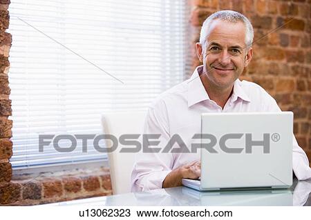 Stock Image - Businessman sitting in office on laptop smiling. Fotosearch