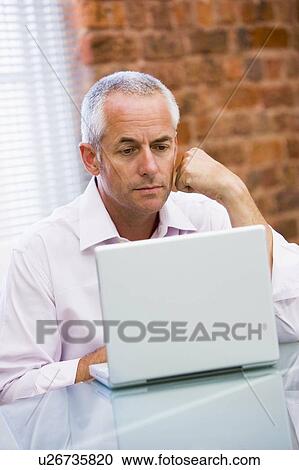 Businessman sitting in office on laptop View Large Photo Image Stock Image - Businessman sitting in office on laptop. Fotosearch