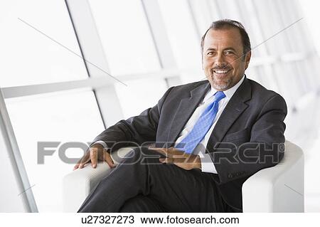 Businessman sitting indoors smiling (high key/selective focus) View Large Photo Image Stock Image - Businessman sitting indoors smiling (high key/selective focus). Fotosearch