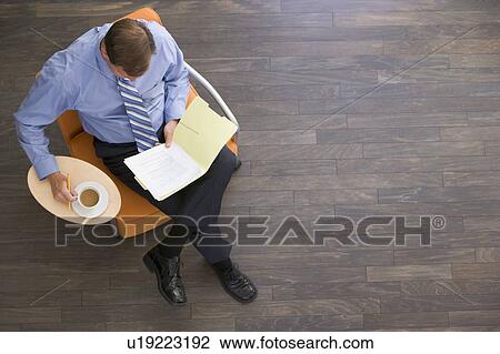 Stock Image - Businessman sitting indoors with coffee and folder. Fotosearch