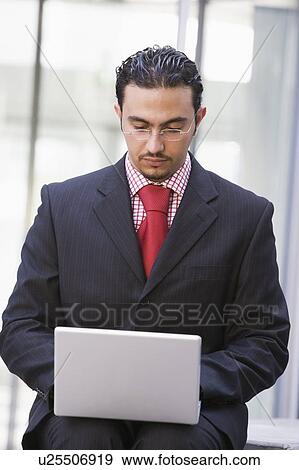 Stock Photo - Businessman sitting outdoors by building with a laptop (high key/selective focus). Fotosearch