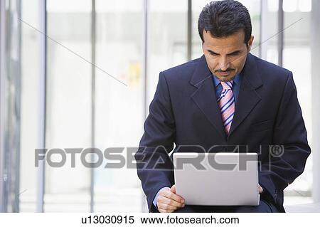 Stock Photography - Businessman sitting outdoors by building with a laptop (high key/selective focus). Fotosearch