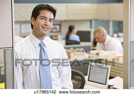 Stock Image - Businessman standing in cubicle smiling. Fotosearch