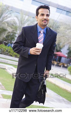 Stock Photo - Businessman walking outdoors with coffee smiling (high key/selective focus). Fotosearch