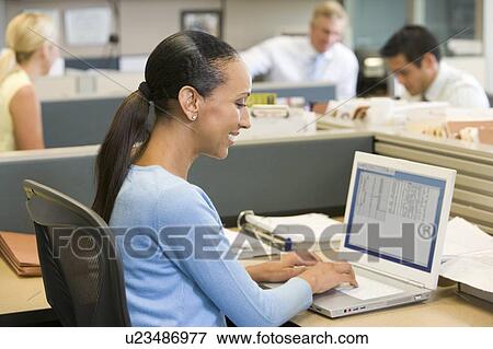 Businesswoman in cubicle using laptop smiling View Large Photo Image Stock Photo - Businesswoman in cubicle using laptop smiling. Fotosearch
