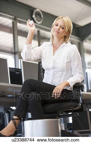 Picture - Businesswoman in office space throwing garbage in bin. Fotosearch