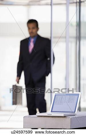 Laptop sitting on stone bench outdoors with businessman walking in background (high key/selective focus) View Large Photo Image Stock Photo - Laptop sitting on stone bench outdoors with businessman walking in background (high key/selective focus). Fotosearch