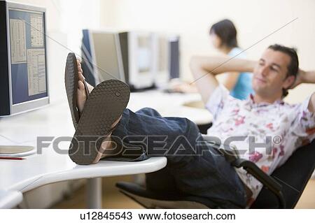Stock Image - Man in computer room with feet up relaxing. Fotosearch