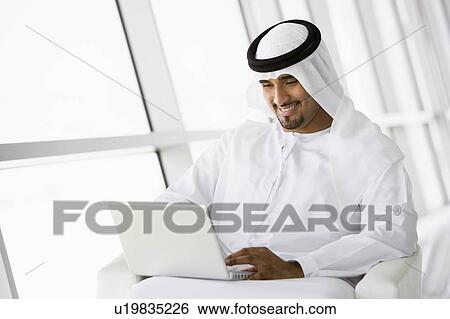 Stock Photograph - Man indoors with laptop smiling (high key/selective focus). Fotosearch
