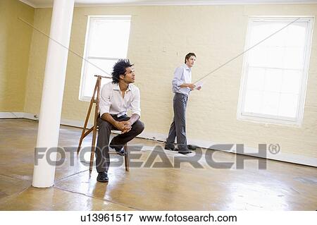 Man sitting on ladder in empty space with another man holding paper View Large Photo Image Stock Photo - Man sitting on ladder in empty space with another man holding paper. Fotosearch