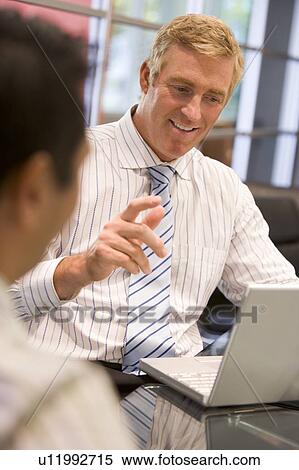 Stock Photography - Two businessmen in boardroom with laptop talking. Fotosearch