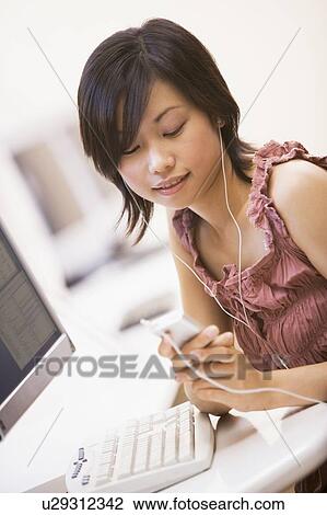 Stock Image - Woman in computer room listening to MP3 player. Fotosearch