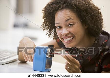 Stock Image - Woman in computer room using pencil sharpener and smiling. Fotosearch