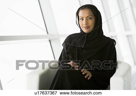 Stock Photo - Woman sitting indoors smiling (high key/selective focus). Fotosearch