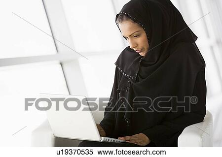 Stock Photography - Woman sitting indoors with laptop (high key/selective focus). Fotosearch