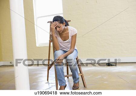 Stock Photo - Woman sitting on ladder in empty space looking tired. Fotosearch