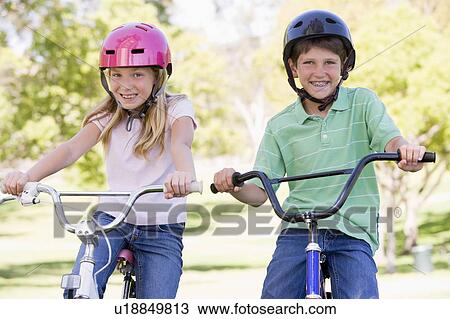 Stock Image - Brother and sister outdoors on bicycles smiling. Fotosearch