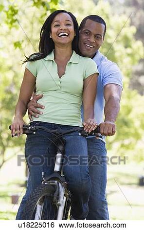 Stock Photograph - Couple on a bike outdoors smiling. Fotosearch