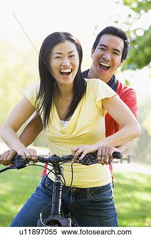 Stock Photography - Couple on a bike outdoors smiling. Fotosearch
