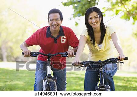 Stock Image - Couple on bikes outdoors smiling. Fotosearch