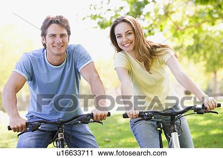 Stock Image - Couple on bikes outdoors smiling. Fotosearch