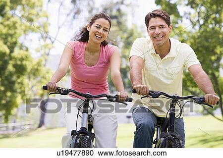 Stock Image - Couple on bikes outdoors smiling. Fotosearch