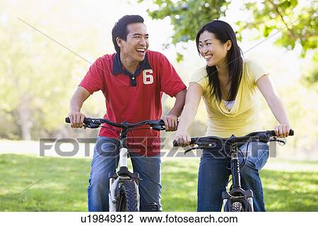 Stock Image - Couple on bikes outdoors smiling. Fotosearch