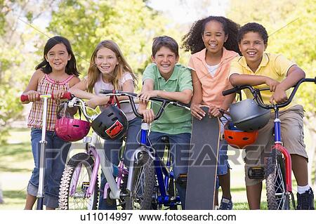 Stock Photo - Five young friends with bicycles scooters and skateboard outdoors smiling. Fotosearch